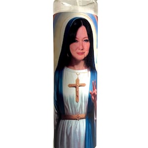 Könnte beinhalten: Eine klare Glas-Kerze mit einem aufgedruckten Bild einer Frau in religiöser Kleidung. Das Bild zeigt einen Kreuzanhänger, ein blau-weißes Gewand und einen Heiligenschein. Die Kerze ist zylindrisch und steht aufrecht.