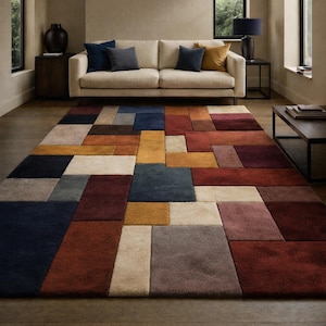 May include: A large, rectangular area rug with a geometric pattern in shades of blue, gold, red, and beige. The rug is placed on a hardwood floor in a living room setting, with a cream-colored sofa and dark accent furniture.