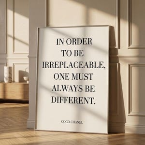 May include: A framed print featuring the quote "IN ORDER TO BE IRREPLACEABLE, ONE MUST ALWAYS BE DIFFERENT." in black text on a cream background. The print is signed "COCO CHANEL". The frame is silver.