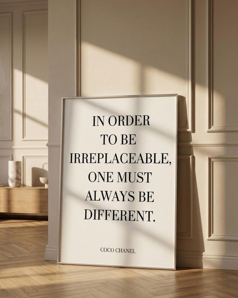 Puede incluir: Impresi&oacute;n enmarcada con la cita "IN ORDER TO BE IRREPLACEABLE, ONE MUST ALWAYS BE DIFFERENT." en texto negro sobre fondo crema. Firmado "COCO CHANEL". El marco es plateado.