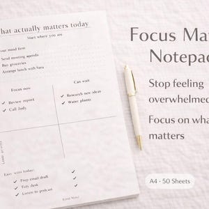May include: A white Focus Matrix Notepad with a pen, designed to help organize tasks. The notepad features a grid layout with sections for tasks, and the text "What actually matters today" and "Focus Matrix Notepad". The notepad is A4 size with 50 sheets.