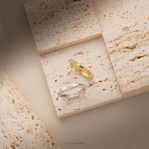 Könnte beinhalten: Zwei dünne Metallringe, einer goldfarben und einer silberfarben. Der goldene Ring ist mit den Namen Hanna und Elias graviert. Der silberne Ring ist mit dem Namen Emma graviert. Beide Ringe haben eine glatte, polierte Oberfläche und ein abgerundetes Band.