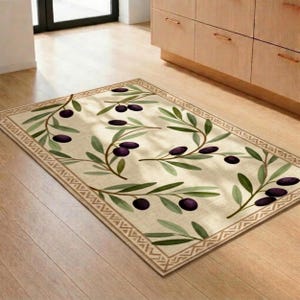May include: A rectangular area rug featuring a cream-coloured background with a repeating pattern of green olive branches and dark purple olives. The rug is framed by a geometric border consisting of a series of interconnected triangles in brown.
