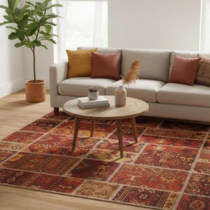 May include: A living room with a beige sofa, cushions, and a round wooden coffee table. A patterned rug in red, orange, and beige tones covers the floor. The rug's patchwork design adds a touch of warmth and visual interest to the room.