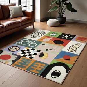 May include: A colorful area rug with a geometric design. The rug features squares of various colors, including green, blue, and pink, each with abstract shapes and patterns. A black and white checkered square is also present.