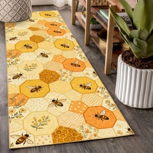 Puede incluir: Una alfombra rectangular con un patrón de panal y abejas. La alfombra presenta formas hexagonales amarillas, naranjas y crema con ilustraciones de abejas y detalles florales. Diseñada para un pasillo o entrada.