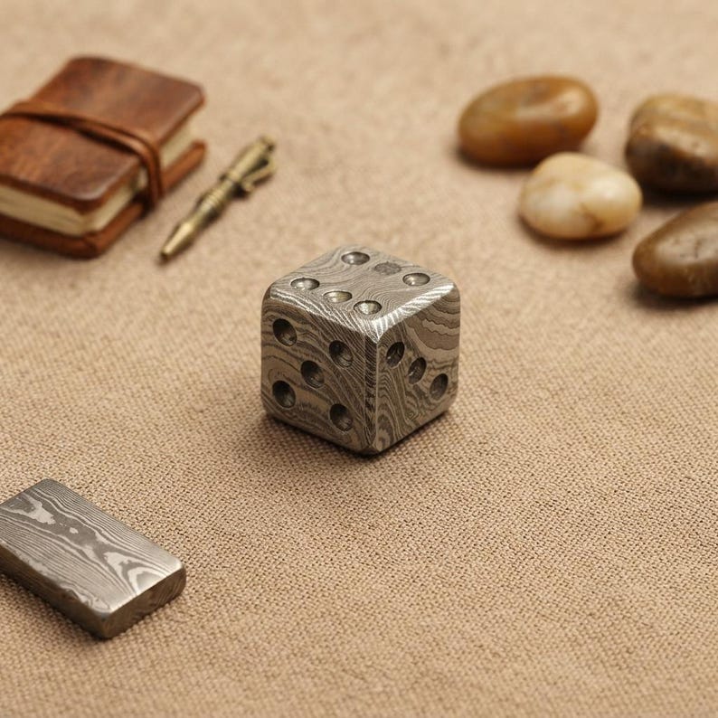 Pu&ograve; includere: Un dado a sei facce realizzato in acciaio di Damasco, caratterizzato da un distinto motivo metallico ondulato e stratificato sulla superficie. Il dado presenta rientranze circolari per i numeri, con una finitura grigio metallizzato e una texture liscia.