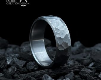 Può includere: Un anello color argento con una superficie martellata e strutturata. Il design dell'anello presenta una serie di sfaccettature geometriche. Il nome del marchio "EXOTIC CREATIONDESIGN" è visibile. L'anello è su sfondo scuro.