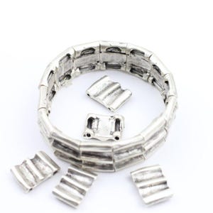 May include: Silver-toned metal bracelet with a textured, ridged design. Several matching decorative pieces are scattered around the bracelet. The bracelet and pieces have a weathered, antique appearance, suggesting a vintage or handcrafted style.