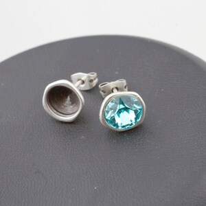 Pode incluir: Um par de brincos de prata com tachas. Um brinco apresenta uma pedra preciosa facetada azul clara. O outro brinco é uma taça de prata. Os brincos são exibidos em uma superfície cinza escuro.