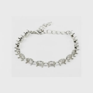 Può includere: Un bracciale in metallo color argento caratterizzato da una serie di castoni ovali vuoti collegati tra loro. Il bracciale include un delicato segmento di catena con una chiusura a moschettone a un'estremità, progettato per pietre.
