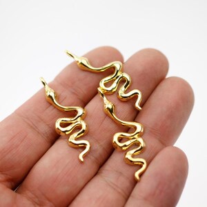 Puede incluir: Amuletos de serpiente dorados con un diseño detallado y serpentino. Los amuletos están en posición enrollada, con una superficie lisa y reflectante. Los amuletos de serpiente son probablemente para la fabricación de joyas o manualidades.