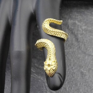 Peut inclure: Une bague dorée en forme de serpent enroulé avec une surface texturée rappelant des écailles. La tête du serpent présente un petit motif découpé en forme de fleur sur le dessus, et le corps s'enroule autour du doigt dans un design ouvert.