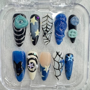May include: A set of ten press-on nails featuring various designs including black and blue bases, spider web patterns, star shapes, a black cat silhouette, swirling glitter lines, and three-dimensional button and circular embellishments.