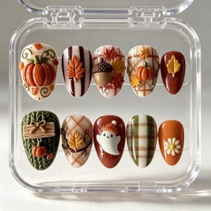May include: A set of ten press-on nails featuring autumn-themed designs including pumpkins, acorns, leaves, a ghost, and plaid patterns in shades of orange, brown, green, and white, all displayed within a clear plastic storage container.