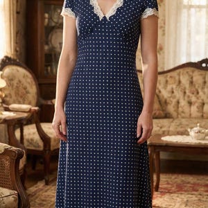 Peut inclure: Une robe bleu marine à pois blancs, avec un décolleté en V et une bordure en dentelle blanche. La robe a des manches courtes et une longueur midi. La femme porte des talons beiges. Le cadre est une pièce de style vintage.