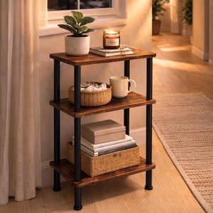 May include: A three-tiered, dark wood side table with black metal supports. The top shelf holds a potted plant, a lit candle, and a book. The middle shelf has a woven basket and a mug. The bottom shelf has boxes and a woven basket.