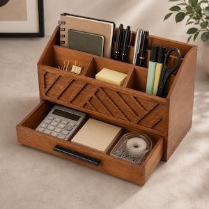 May include: A brown wooden desk organizer featuring a pull-out drawer with a black handle, multiple upper compartments for stationery, and a front panel with a diagonal slat pattern. It holds a calculator, notebooks, pens, scissors, and clips.