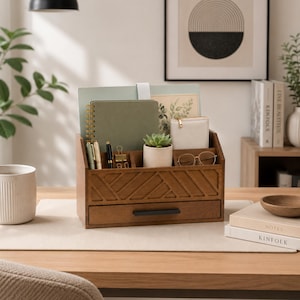 May include: A wooden desk organizer featuring a geometric carved front panel, multiple upright slots for notebooks and papers, small compartments for pens and accessories, a central potted succulent, and a single drawer with a black metal handle.