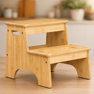 May include: A two-step stool constructed from light-colored bamboo wood. The stool features a rectangular top step and a lower step, with arched cutouts at the base of the side panels and a handle cutout on the upper side panel for portability.