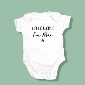 Może przedstawiać: Biały śpioszek dla niemowlęcia z czarnym napisem "Hello World I'm Mac" i czarną gwiazdką.
