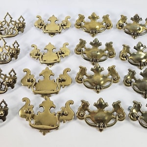 May include: A selection of antique brass drawer pulls in various designs. The pulls have ornate detailing and a warm, aged finish. Suitable for restoring vintage furniture or adding a touch of classic style to cabinets and drawers.