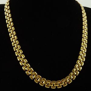 May include: A gold-coloured necklace with a linked design. The necklace is composed of rectangular links, creating a textured and reflective surface. The jewellery is displayed against a black background.