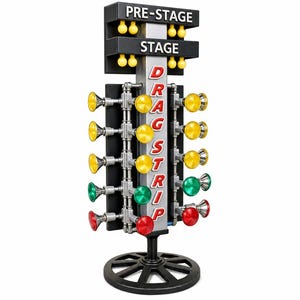 May include: A drag strip Christmas tree starting light display featuring a vertical silver post with the text DRAG STRIP in red letters. It includes top PRE-STAGE and STAGE light bars, and multiple rows of yellow, green, and red circular lights.