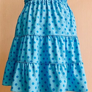 May include: A blue skirt with white polka dots and a tiered design. The skirt has an elastic waistband.