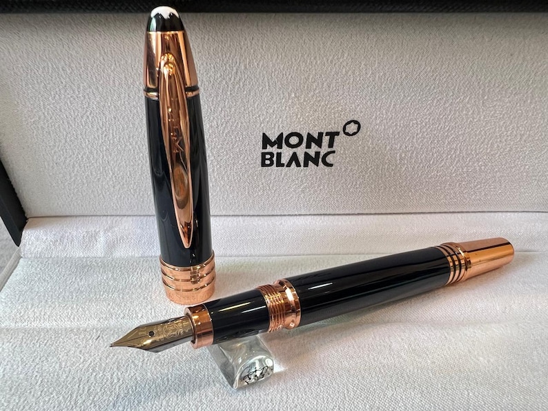 May include: A black and rose gold Montblanc fountain pen, with the cap removed. The pen is presented in its original box, with the Montblanc logo displayed. The pen features a sophisticated, elegant design.