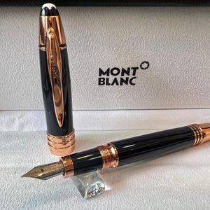 May include: A black and rose gold Montblanc fountain pen, with the cap removed. The pen is presented in its box, with the Montblanc logo. The pen has a sleek, elegant design, with a rose gold nib.