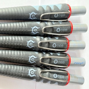 Op de afbeelding: Een close-up van vijf zwarte pennen met zilveren clips en rode accenten. Elke pen heeft een getextureerde grip, een zilveren punt en een logo. De pennen zijn parallel gerangschikt, met de punten naar rechts gericht.