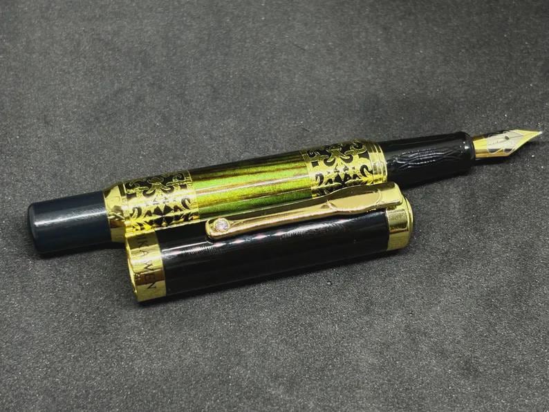 May include: A black and gold fountain pen with a decorative design on the barrel. The pen has a gold nib and a gold clip. The cap is partially removed, revealing the pen's design.
