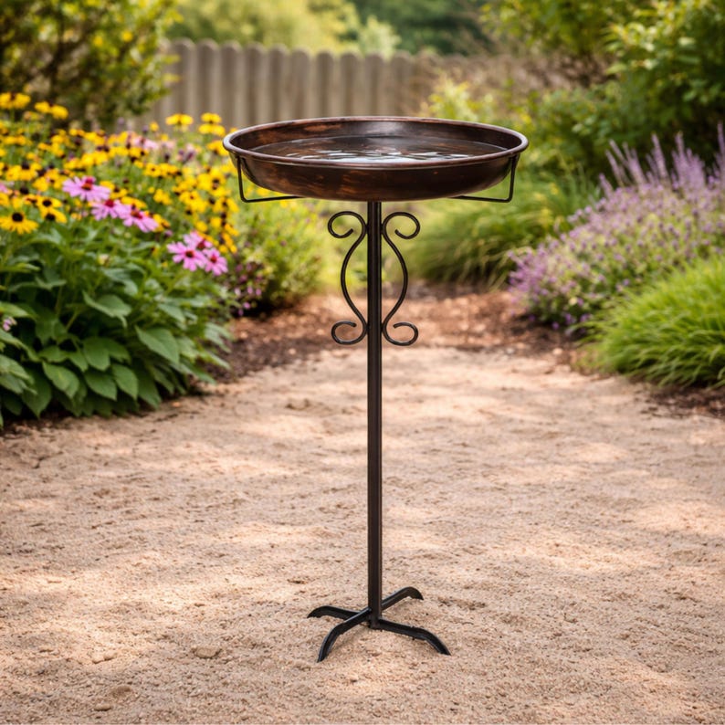 Peut inclure: Un abreuvoir &agrave; oiseaux en bronze avec une cuvette ronde, soutenu par un support en m&eacute;tal d&eacute;coratif. Le support pr&eacute;sente un design orn&eacute; et une base &agrave; trois branches. L'abreuvoir est rempli d'eau et est install&eacute; dans un jardin. Hauteur: environ 76 cm.