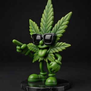 Peut inclure: Figurine en forme de feuille de cannabis verte, portant des lunettes de soleil noires, avec la langue tirée et un geste de pointage. La figurine est posée sur une base en marbre noir et blanc. Design de type dessin animé.
