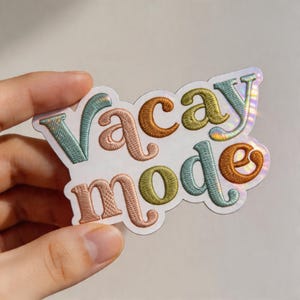 May include: A colorful sticker with the words "Vacay Mode" in a retro font. The text is embroidered with various colors, including teal, orange, and yellow. The sticker has a holographic border.