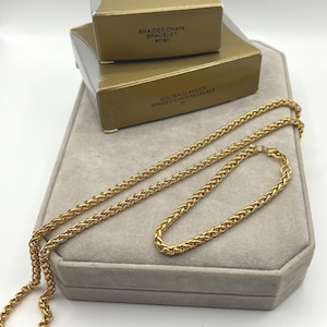 Può includere: Una collana a catena intrecciata color oro e un bracciale a catena intrecciata abbinato. I gioielli sono presentati con due scatole color oro etichettate AVON, BRAIDED CHAIN BRACELET small e GOLDEN CLASSICS BRAIDED CHAIN NECKLACE 20 inches.