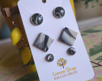 May include: A white card displays four pairs of resin and clay earrings with silver-colored metal posts. The earrings feature black, white, and gold marbled designs. The card also has the text "Lemon Drop Resin & Clay Jewellery".