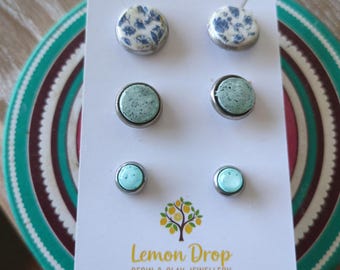 May include: Three pairs of stud earrings on a white card. The top pair has a white and blue floral design, the middle pair is a speckled teal, and the bottom pair is a solid teal. The card has the text "Lemon Drop Resin & Clay Jewellery".