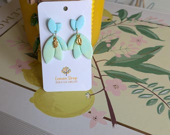 Pendientes colgantes de arcilla polimérica en dos tonos de aguamarina y verde con forma de pétalo y un detalle de pan de oro. Hechos a mano.