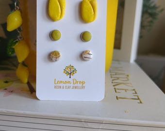 May include: A white card displays six pairs of stud earrings in yellow, green, and white. The earrings are shaped like tulips, circles, and small patterned designs. The card has the text "Lemon Drop Resin & Clay Jewellery".