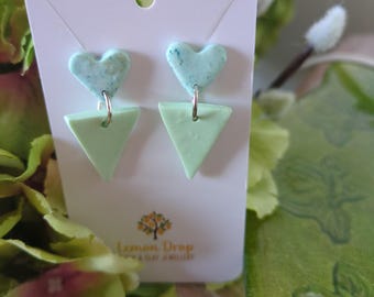 May include: A pair of handmade earrings on a white card. Each earring features a light green triangle and a heart-shaped top with blue speckles. The card has the text "Lemon Drop" and a logo.