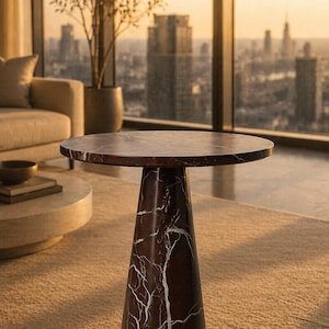 May include: A round, dark brown marble side table with a white veined pattern. The table has a conical base and is set on a beige carpet. The background features a cityscape and a large window.