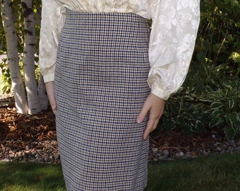 May include: A knee-length skirt with a classic houndstooth pattern in navy blue, tan, and white. The skirt is paired with a cream-colored blouse with a floral pattern. The outfit is suitable for a professional or casual setting.