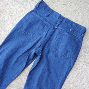 May include: Dark blue denim jeans with two back pockets and a Wrangler label. The jeans have a classic five-pocket design and a straight leg cut. The denim appears to be a medium weight.
