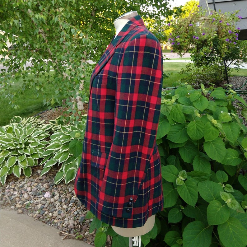 May include: A red, green, and yellow plaid blazer. The blazer has a double-breasted closure and a single button on each cuff.