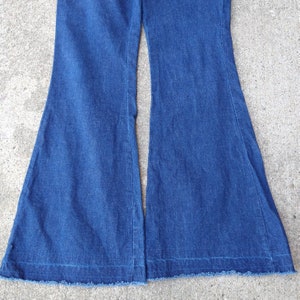 May include: A pair of blue denim bell-bottom pants. The pants have a classic five-pocket design and a wide, flared leg. The hemline is frayed. The pants are made of a medium-weight denim fabric.