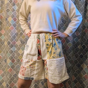 May include: Patchwork shorts with a mix of floral, corduroy, and patterned fabrics in cream, yellow, red, and blue. The shorts have an elastic waistband and a relaxed fit, showcasing a unique, handcrafted design.