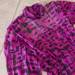 May include: A vibrant magenta dress with a high neckline and long sleeves. The sheer fabric features a geometric pattern in black and magenta. The dress appears to be made of a lightweight material, suitable for warmer weather.