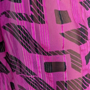 May include: A sheer, magenta fabric with a repeating pattern of black, brown, and gold geometric shapes and vertical stripes. The fabric has a delicate, flowing appearance, with light reflecting off the gold accents.